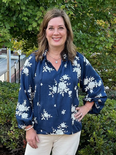 Add to your wardrobe with our Embroidered Ruffle Tie Neck Blouse! This stunning navy top features beautiful cream embroidery and long elastic-cuffed sleeves. The ruffled neck with tie adds a touch of elegance and pairs perfectly with cream pants. Dress it down with jeans for a fun and stylish look.

Material: 100% Polyester&nbsp;

Care Instructions: Hand wash separately in cold water, lay flat to dry