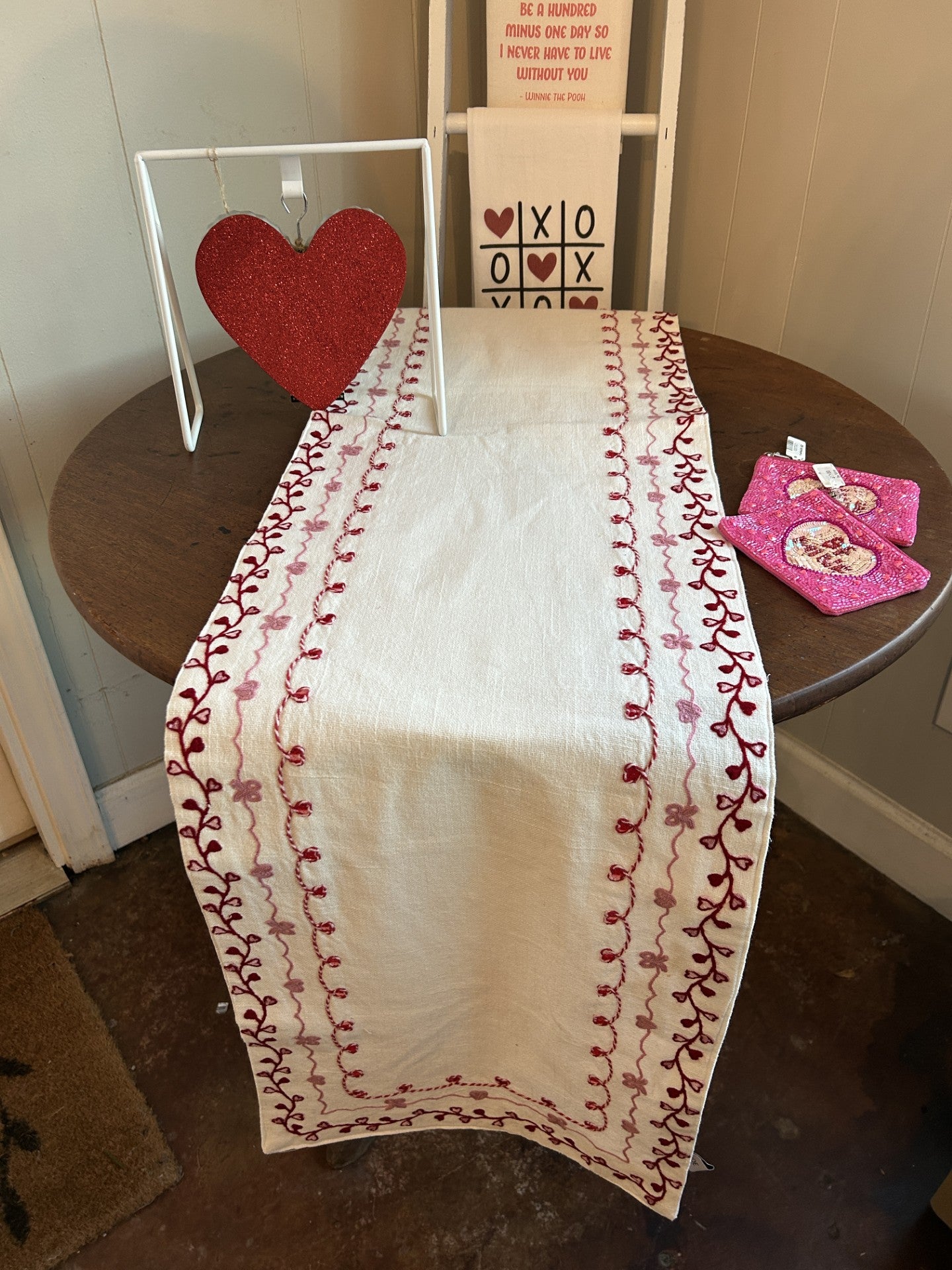 Bring timeless elegance to your Valentine's Day table with this exquisite runner. Set against a pristine white background, an enchanting embroidered border in soft pinks and rich reds creates a romantic focal point that captivates at first glance. The intricate needlework detail adds sophistication and handcrafted charm to your dining experience. Whether you're hosting an intimate dinner or a festive gathering, this stunning piece transforms your table into a declaration of love and impeccable taste that yo
