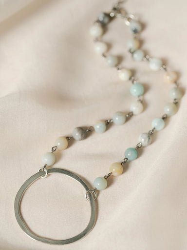 This stunning Selena necklace features a hammered silver metal circle pendant, accented by round Amazonite beads. The combination of brass and bead chain adds a touch of elegance to this piece.

16" long with 2" extender

Care Instructions: Avoid water, soap, and harsh chemicals. Store in a box or bag in a cool, dry place. Clean using a dry soft cloth.