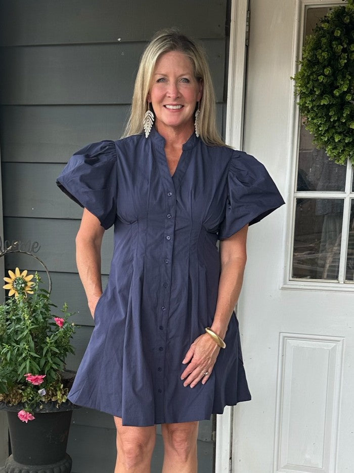 This button-front dress features a flattering silhouette and charming short puffed sleeves, perfectly balancing style and comfort. Designed with convenient side pockets, it’s as practical as it is chic. Whether you're gearing up for game day or heading out for a fun evening, this dress ensures you look effortlessly put-together and ready to enjoy every moment.

Material: 100% Cotton; Lining: 100% Polyester

Care Instructions: Hand wash cold, hang to dry