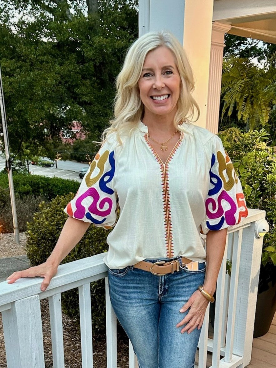 You will love our ruffled collar top featuring a cream background that highlights its stunning embroidered puffed sleeves. The vibrant Fall accent colors add a warm, seasonal touch, making it perfect for stylish autumn outings. Designed to blend classic charm with eye-catching details, this top effortlessly enhances your look with a unique, feminine flair.

Cindy is wearing a size Medium. She paired it with our "Risen High Rise-Wide Baggy Jeans in Dark". She accessorized with