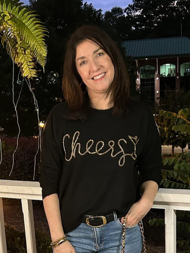 Celebrate the season in style with this black long sleeve sweater featuring elegant gold "Cheers" script across the front. Lightweight and comfortable, it’s perfect for festive gatherings without feeling bulky. Add a touch of holiday cheer to your wardrobe with this fun yet chic sweater that effortlessly combines comfort and festive flair.

Material: 61% Polyester / 15% Acrylic / 15% Nylon / 6% Wool / 3% Spandex

Care Instructions: Hand wash cold, line dry