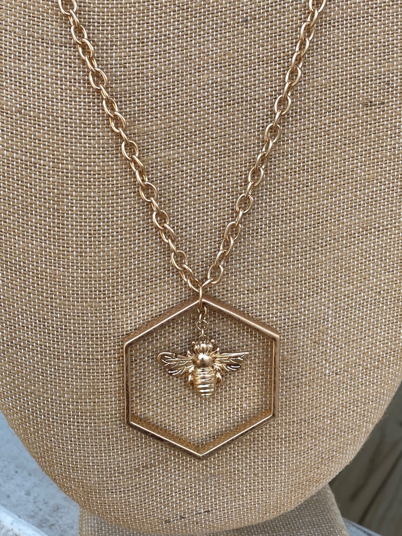 This luxurious necklace features a glossy queen bee drop nestled inside a hexagon and hung on a long gold chain, perfect for any elegant look. With an adjustable length of 30-33", you can show off your inner beehive queen all day long.