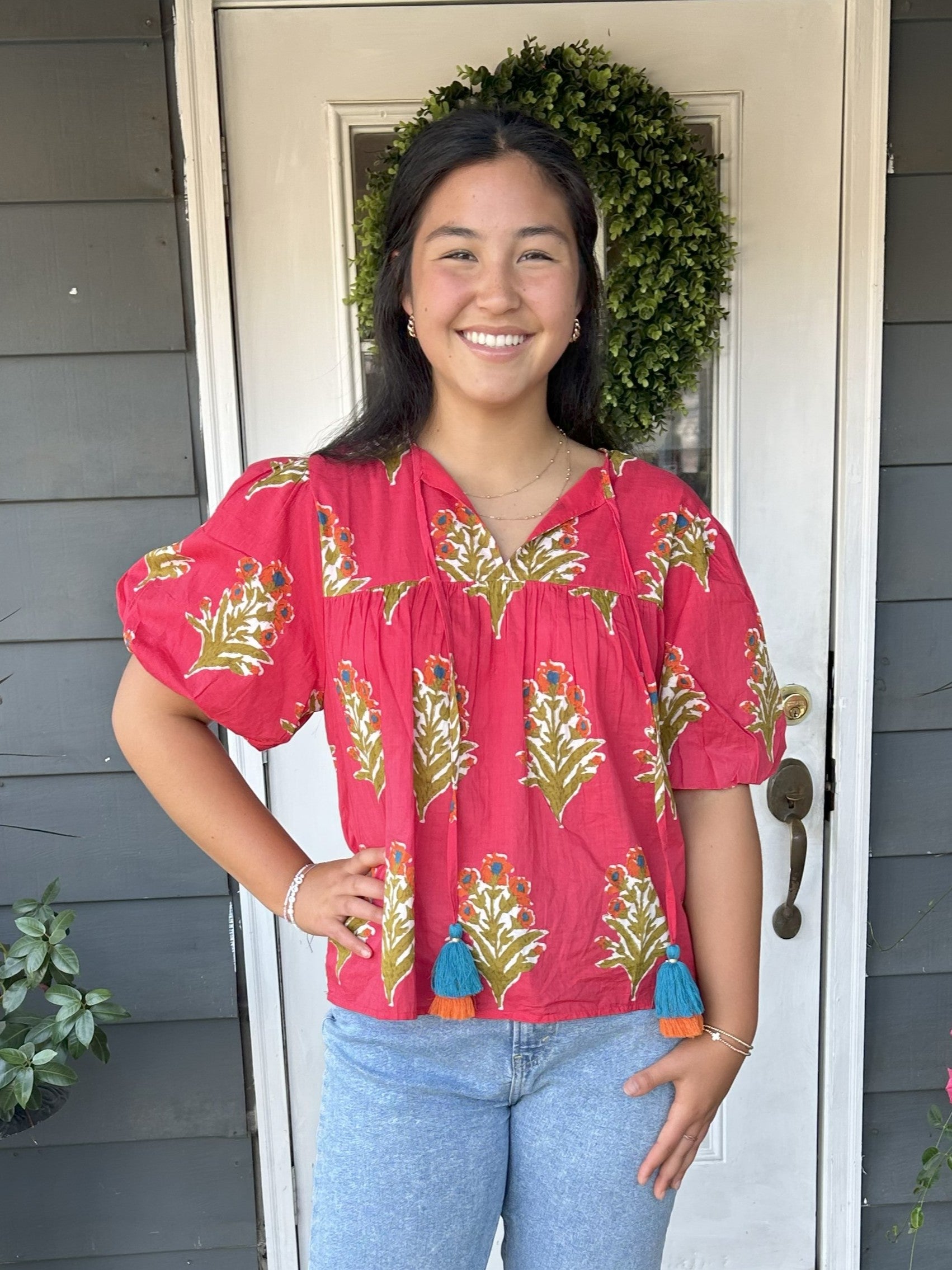 This Puff Sleeve Front Tie Top features charming puffed short sleeves and a gathered bodice that flatters every figure. The cute front tie with tassels adds a playful touch, set against a vibrant red background adorned with a beautiful floral print. Perfect as a stylish transition piece, it effortlessly bridges warm summer days into crisp fall evenings.

Material: 100% Cotton

Care Instructions: Gentle cool hand wash, dry flat
