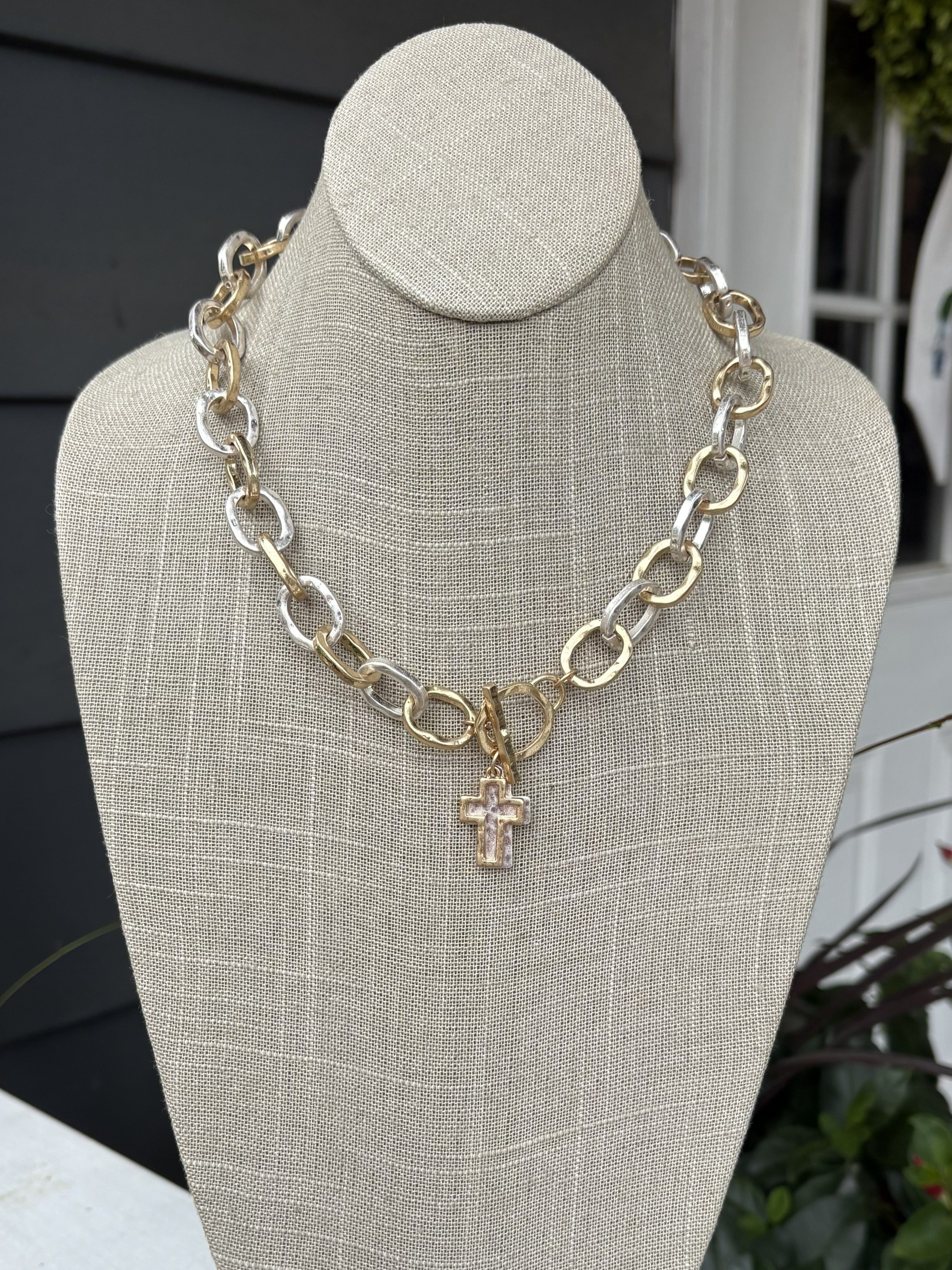 This mixed metal chain link necklace combines understated sophistication with everyday versatility. Two cross charms dangle gracefully from uniquely textured chain links, creating visual interest that works with any outfit. The T-bar closure provides secure, comfortable wear, while the mixed metal finish ensures effortless coordination with your existing jewelry collection. Perfect for layering or wearing solo, this piece brings timeless charm to any ensemble.
