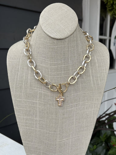 This mixed metal chain link necklace combines understated sophistication with everyday versatility. Two cross charms dangle gracefully from uniquely textured chain links, creating visual interest that works with any outfit. The T-bar closure provides secure, comfortable wear, while the mixed metal finish ensures effortless coordination with your existing jewelry collection. Perfect for layering or wearing solo, this piece brings timeless charm to any ensemble.