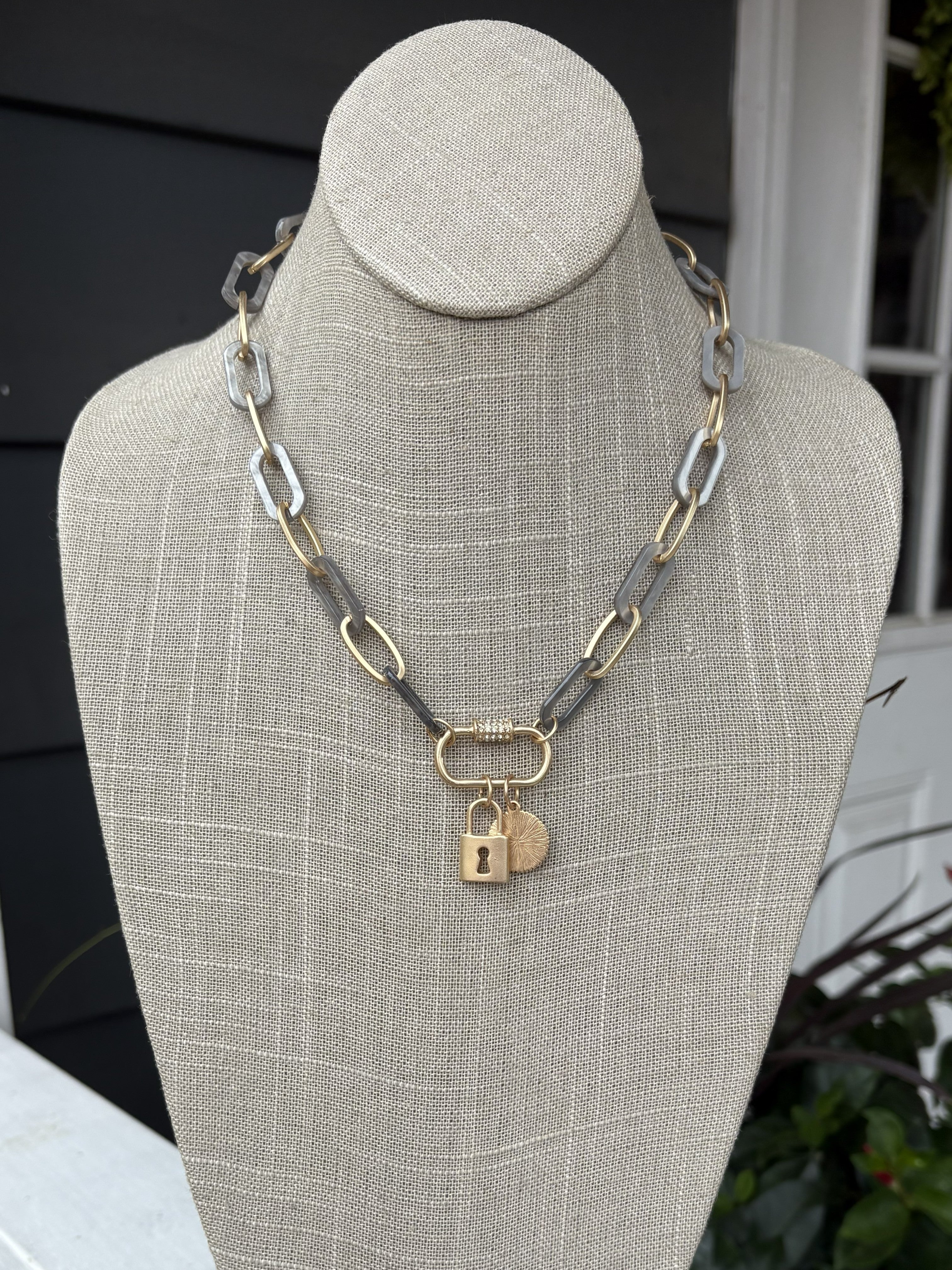 This short gray and gold chain necklace is a versatile essential for any jewelry collection. The eye-catching rhinestone-embellished lock pendant adds intrigue and glamour, while the delicate chain keeps the overall look refined. Layer it with other pieces for a curated aesthetic, or wear it alone to let the pendant shine. Perfect for transitioning from day to night.