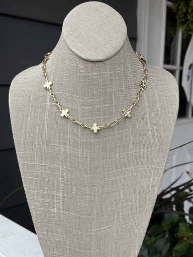 Delicate gold chain adorned with textured gold crosses creates an understated yet sophisticated look. Perfect for layering or wearing alone, this necklace combines minimalist design with timeless elegance. The short length offers versatile styling options for any occasion.