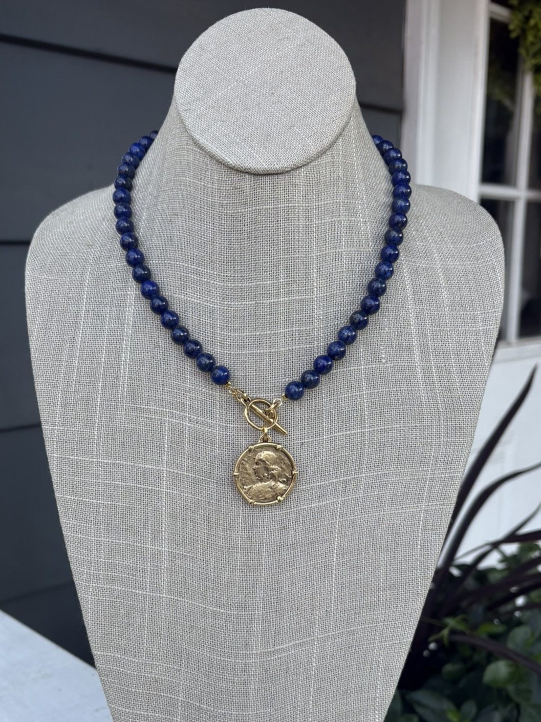 This dark blue beaded necklace showcases a captivating coin pendant that brings depth and character to any outfit. Each bead is carefully hand-strung to create a refined, textured look that works beautifully on its own or layered with other pieces. The secure T-bar closure provides a comfortable, reliable fit for all-day wear. Whether you're dressing up for an evening out or adding polish to casual wear, this versatile necklace effortlessly bridges your day and night wardrobe.