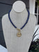 This dark blue beaded necklace showcases a captivating coin pendant that brings depth and character to any outfit. Each bead is carefully hand-strung to create a refined, textured look that works beautifully on its own or layered with other pieces. The secure T-bar closure provides a comfortable, reliable fit for all-day wear. Whether you're dressing up for an evening out or adding polish to casual wear, this versatile necklace effortlessly bridges your day and night wardrobe.