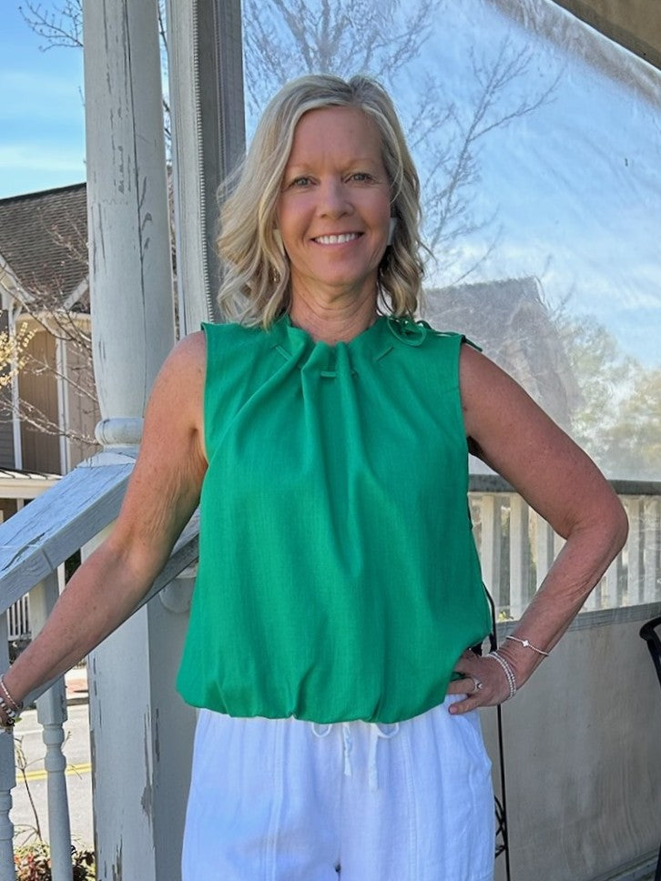 This versatile sleeveless top features a charming tie-gathered neckline and cinched waist for a flattering silhouette. Perfect for spring and summer occasions, it pairs effortlessly with jeans or casual pants for laid-back style. The soft rayon-polyester blend offers comfort and breathability. Ideal for St. Patrick's Day celebrations or everyday wear.&nbsp;

Material: 70% Rayon / 30% Polyester

Care Instructions: Gentle cool hand wash, dry flat
