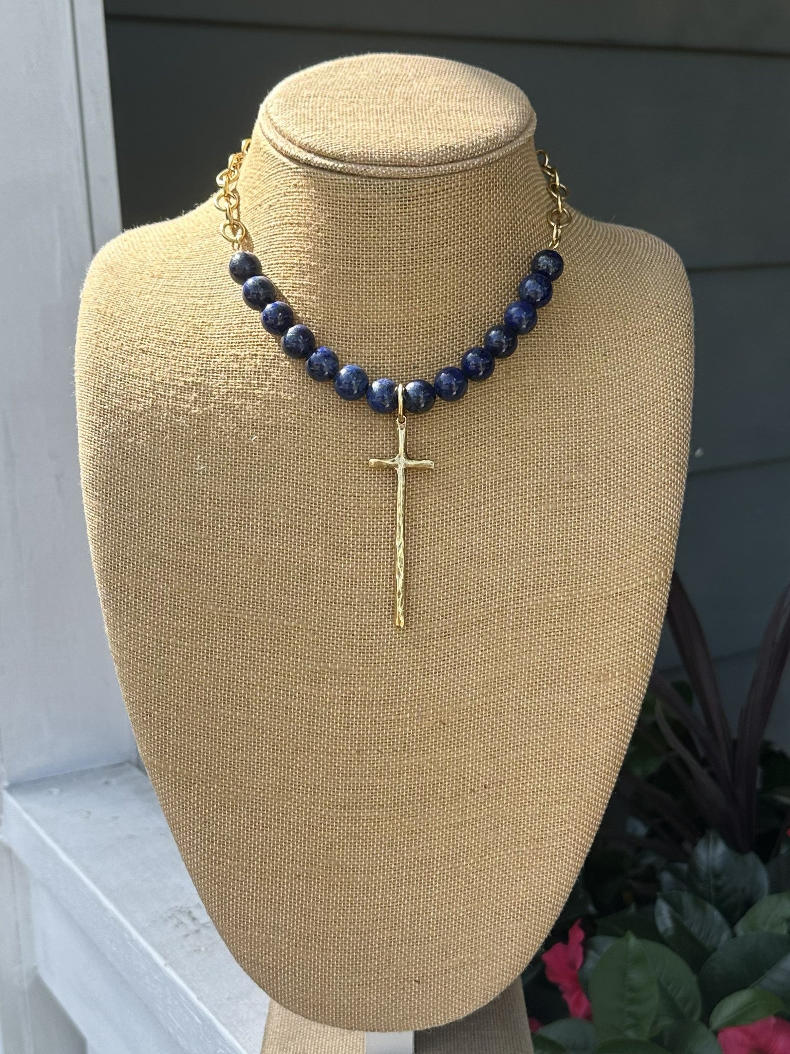 Elegant bead and chain necklace featuring rich lapis beads paired with delicate open gold chain. The centerpiece showcases a long, hammered cross pendant with beautiful texture and dimension. A sophisticated piece that combines natural stone beauty with refined metalwork for a timeless look.

Approximate length: 19-21"