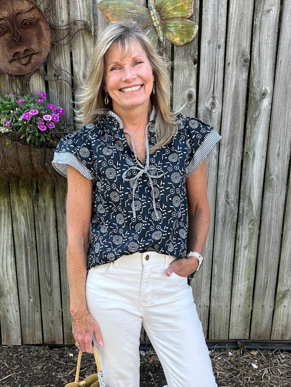 This versatile top combines feminine details with everyday wearability. Ruffled cap sleeves and a tie neckline with coordinating ruffles bring texture and movement, while the navy and white striped trim against the navy fabric creates a crisp, classic contrast. Style it with white pants, shorts, or your favorite denim for a super cute summer outfit! Looks great untucked, tucked or just front tucked.

Carolee is wearing a Small.

Material: 100% Cotton

Care Instructions: Hand wash cold, hang to dry