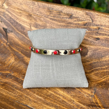 Bring bold energy to every moment with the Mada Gold, Red &amp; Black Bangle Bracelet. Whether you're celebrating game day or adding everyday flair, this versatile piece shines worn solo or stacked for maximum impact. The striking color palette and timeless bangle design make it an essential accessory for anyone who loves to mix style with spirit.