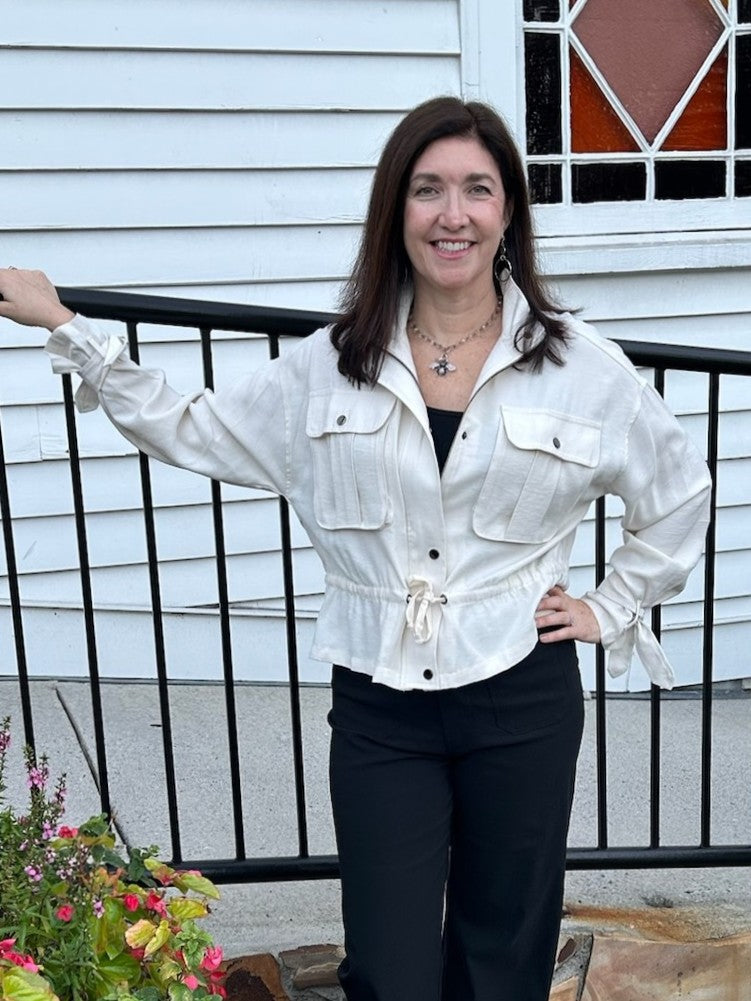 A wardrobe essential that works as hard as you do. This cream utility jacket combines effortless style with practical design. The soft fabric drapes beautifully while the stand-up collar and zip front with snap placket deliver contemporary edge. Drawstring waist cinches for a flattering silhouette, and adjustable tie cuffs at the wrists ensure a perfect fit every time. Long sleeves provide coverage, while the neutral tone makes it the perfect layer for any season or occasion.