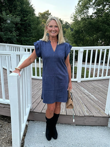 Elegance in a softly structured silhouette. This navy faux suede dress features a flattering V-neckline, delicate cap sleeves, and refined stitch detailing that adds subtle texture without overwhelming the design. The plush fabric drapes beautifully, making it an ideal choice for casual outings or dressed-up occasions.