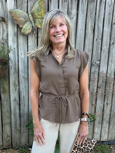 Timeless style meets everyday comfort in this brown button-down top. The adjustable tie waist creates a flattering, customizable fit that works for any body type. Crisp front placket, structured collar, and cap sleeves deliver a polished look that pairs beautifully with everything in your wardrobe. Whether dressed up for the office or down for weekend wear, this neutral essential is the foundation piece every closet needs.

Material: 65% Rayon / 35% Nylon

Care Instructions: Machine wash cold, line dry