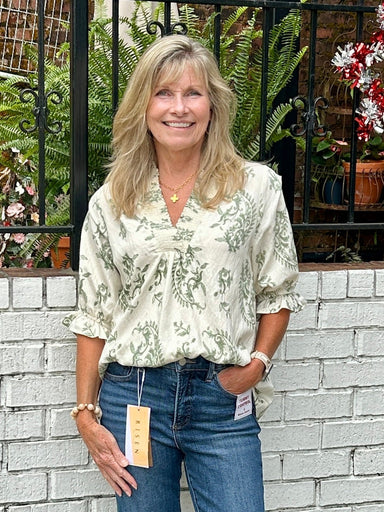 Carolee is wearing an Umgee cotton top in cream with a sweet print in mossy green. She is wearing Risen jeans and sandals.  