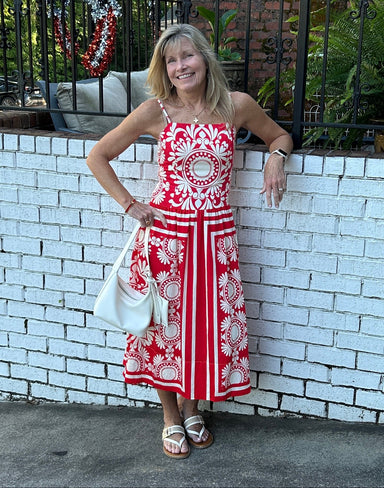 Carolee is wearing a red & Ivory print sundress with a cute white bag and sandals. The midi dress has an awesome print. rushing in the back and spaghetti strapts.  She is wearing a small.