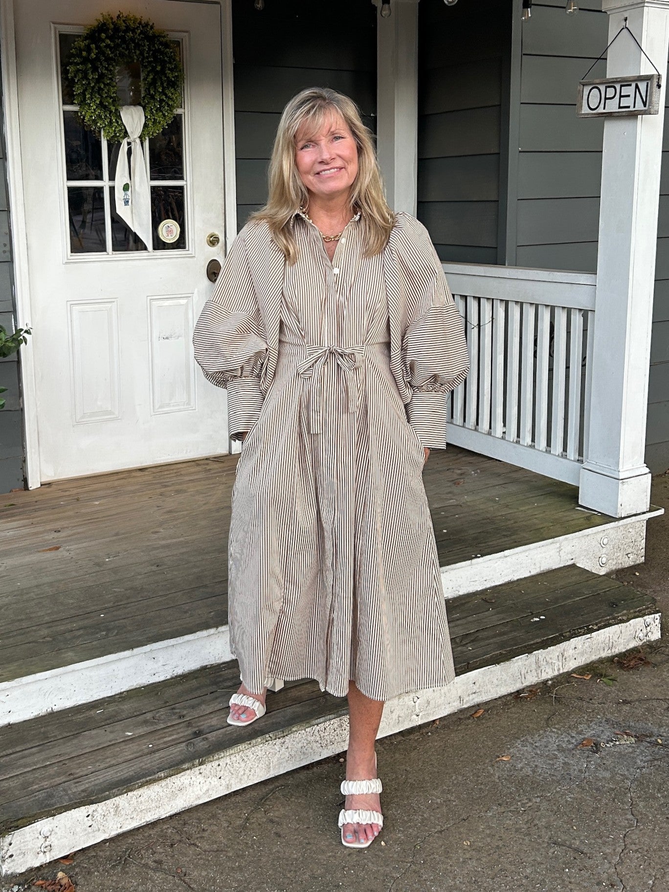 Effortless style meets playful details in this brown stripe midi dress. Voluminous balloon sleeves add romantic charm, while the button-front design and tie waist give you complete control over your silhouette. Lined for comfort and confidence, this versatile piece transitions seamlessly from casual daytime looks to an evening of dinner.

Carolee is wearing a size Small.

Material: 65% Cotton / 32% Nylon / 3 Spandex: Lining: 100% Cotton

Care Instructions: Hand wash cold, line dry