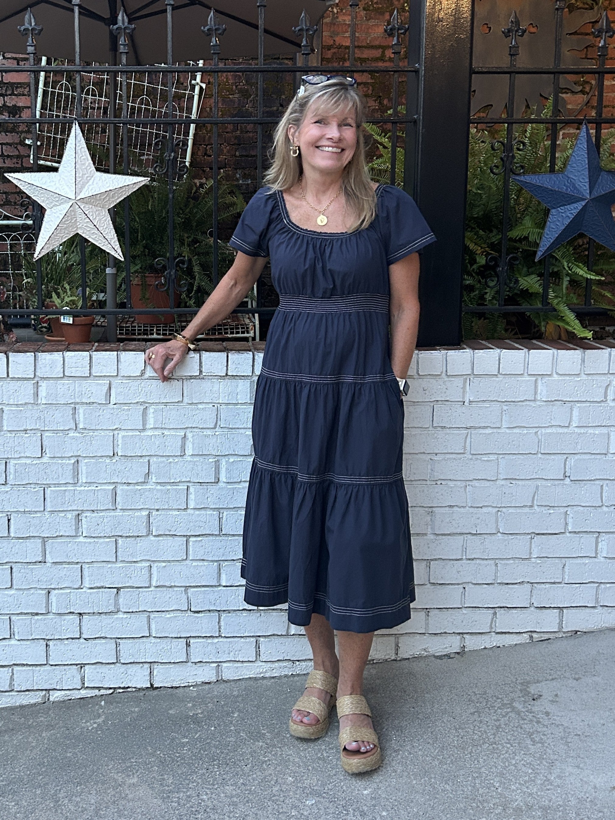 Casual meets game-day style in this smocked-waist tiered midi dress. The navy silhouette features contrasting stitching and a flattering tiered skirt that moves beautifully. The fabric is soft and comfortable. Short sleeves keep it casual and comfortable, while the defined waist creates a polished shape. Layer with a jacket to take it further into fall.&nbsp;

Carolee is wearing a small. She paired it with sandals and boots.

Material: 100% Cotton

Care Instructions: Hand wash with cold water, hang dry