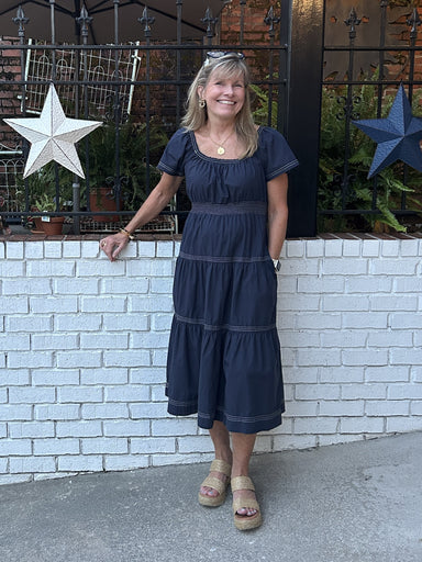 Casual meets game-day style in this smocked-waist tiered midi dress. The navy silhouette features contrasting stitching and a flattering tiered skirt that moves beautifully. The fabric is soft and comfortable. Short sleeves keep it casual and comfortable, while the defined waist creates a polished shape. Layer with a jacket to take it further into fall.&nbsp;

Carolee is wearing a small. She paired it with sandals and boots.

Material: 100% Cotton

Care Instructions: Hand wash with cold water, hang dry