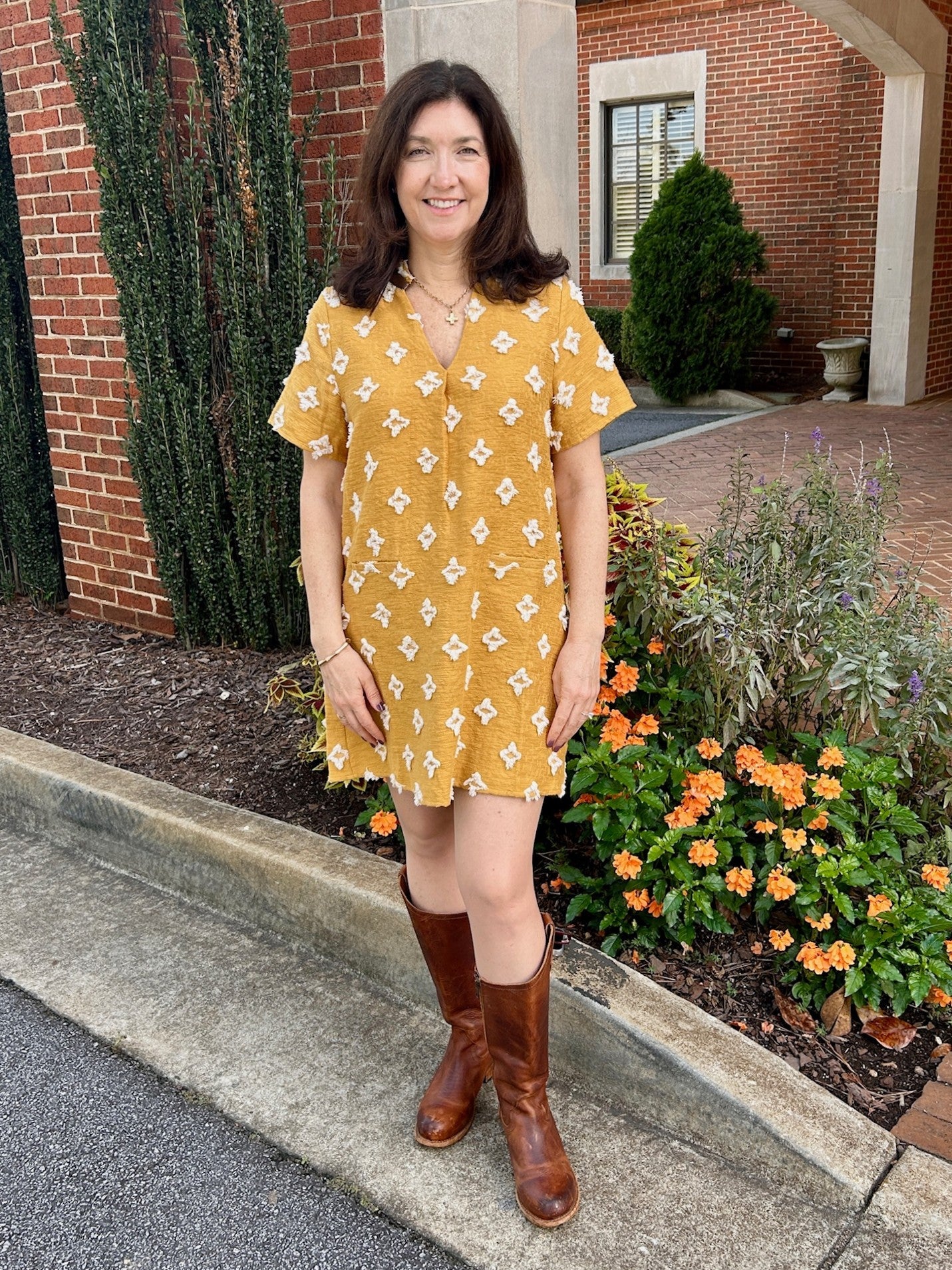 Stand out at GA Tech events in this Short Sleeve V-Neck Dress, crafted from textured material with a beautiful mustard color. The dress features tufted, contrasting detailing and a faux leather trim around the neck for a polished finish. Fully lined for comfort, it combines style and sophistication effortlessly, making it a perfect choice to showcase your college spirit with elegance.

Tara is wearing a size Medium. She added our "Maryna Chain Link Cross Necklace".

Material: 100% Cotton

Care Instructions: