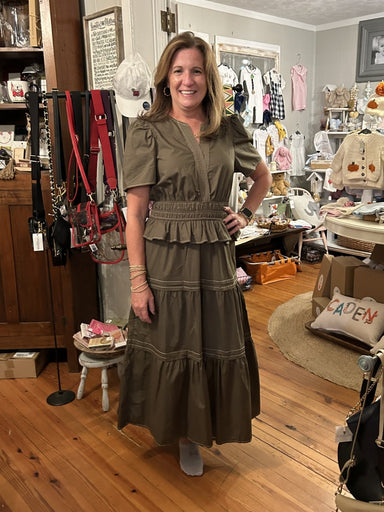This dark olive green tiered midi dress combines comfort and style effortlessly. Featuring a flattering V-neck and short sleeves, it highlights stitched detailing for subtle elegance. The cinched waist ensures a great fit that accentuates your silhouette, while the tiered skirt adds movement and charm. Perfect for any occasion, this dress offers a sophisticated yet relaxed look.

Material: 100% Cotton; Lining: 100% Polyester

Care Instructions: Gentle cool hand wash, dry flat