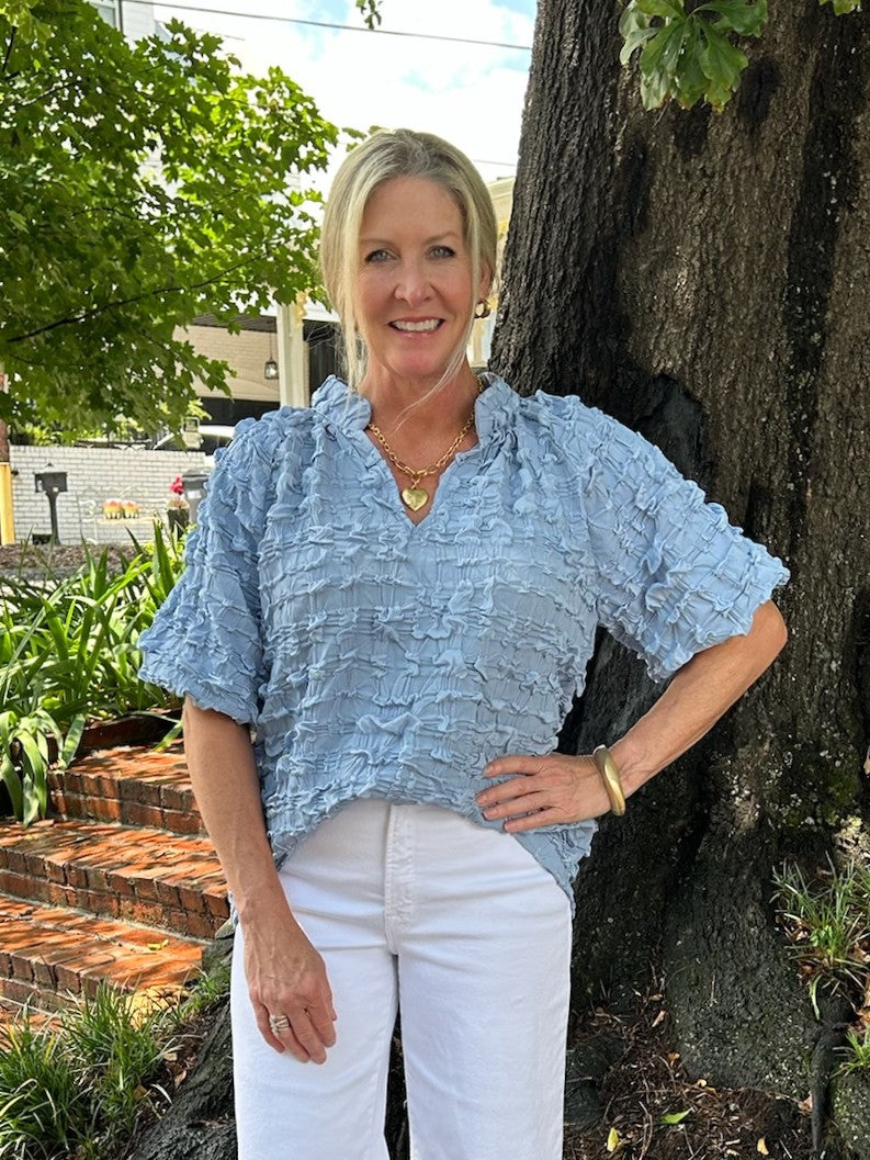 Enhance your wardrobe with our Textured Ruffle Top featuring a flattering V-neckline.. The gorgeous light blue hue and puffed sleeves add a touch of romance. The textured fabric provides dimension, and is perfect for both casual outings and dressier occasions.

Coleen is wearing a size small.

Material: 100% Polyester

Care Instructions: Hand wash cold, hang to dry