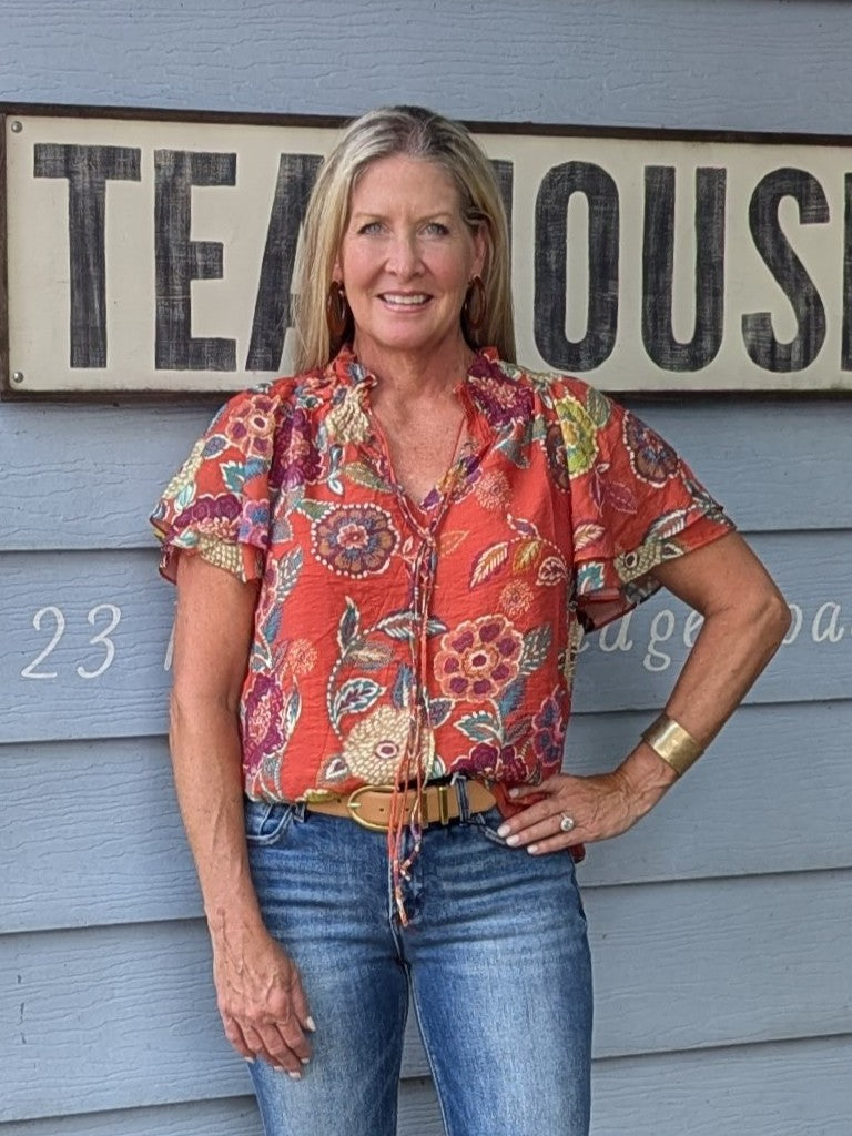 Capture the essence of autumn with the Flutter Sleeve Floral Front Tie Top. Designed with double flutter sleeves and a double front tie, it creates a flattering shape with graceful movement. The ruffled elastic neckline adds a soft, feminine detail, while the lined fabric guarantees comfort and modesty. Ideal for transitioning your wardrobe, this top combines effortless style with everyday ease.

Coleen is wearing a size Small. She paired the top with our Low Rise-Flare Jeans - Dark. She accessorized with o