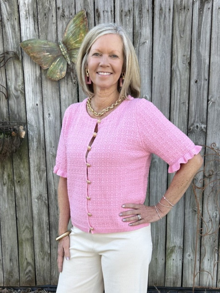This pink knitted top is your answer to effortless style. The soft, textured weave feels luxurious against your skin, while gleaming gold buttons add a touch of sophistication. Ruffle-trimmed short sleeves bring playful charm to every outfit. Wear it buttoned up for a polished day look, or drape it open over a camisole for evening elegance. Whether you're dressing down with jeans or dressing up for a night out, this versatile piece adapts to your lifestyle—making it the wardrobe investment you've been waiti