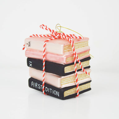 Celebrate your passion for literature with this enchanting hand-painted ornament shaped like a charming stack of books. Rendered in soft pinks and classic black tones, it's finished with a delicate striped ribbon that captures the cozy warmth of a beloved bookshelf. Perfect for book lovers and reading enthusiasts, this whimsical piece brings literary charm to any holiday display or year-round décor collection.