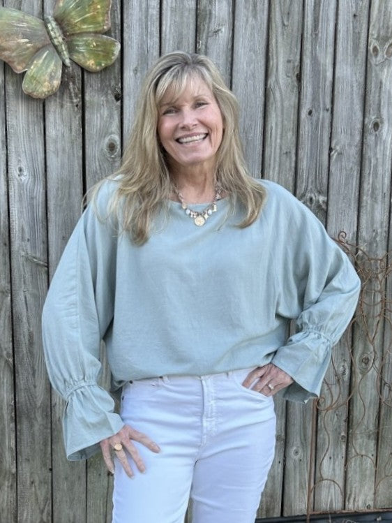 Discover the perfect blend of comfort and style with this linen dolman sleeve blouse. Rendered in a soft light sage tone, it features a graceful wide crew neckline and flowing dolman sleeves that move with you throughout your day. The lightweight linen fabric keeps you cool and comfortable, while charming full ruffled cuffs add a delightful finishing touch.&nbsp;

Material: 78% Rayon / 22% Linen

Care Instructions: Machine wash cold, line dry