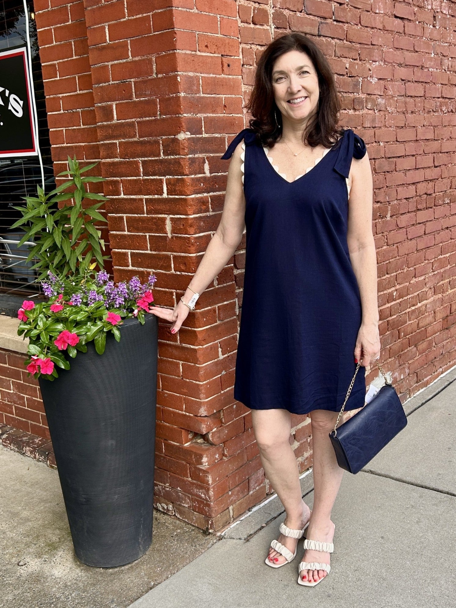 This adorable navy sleeveless dress features charming tie shoulder straps and playful contrasting ric rac trim along the neck and arms. Its versatile design easily transitions from day to night—simply switch up your shoes to suit the occasion. Perfect for adding a cute, stylish touch to any wardrobe.

Tara is wearing a size small. She added our lovely First Love Slip On High Heel, and our Ahdorned Small Flap Bag with Chain in navy.

Material: 30% Linen / 70% Rayon; Lining: 100% Polyester

Care Instructions: