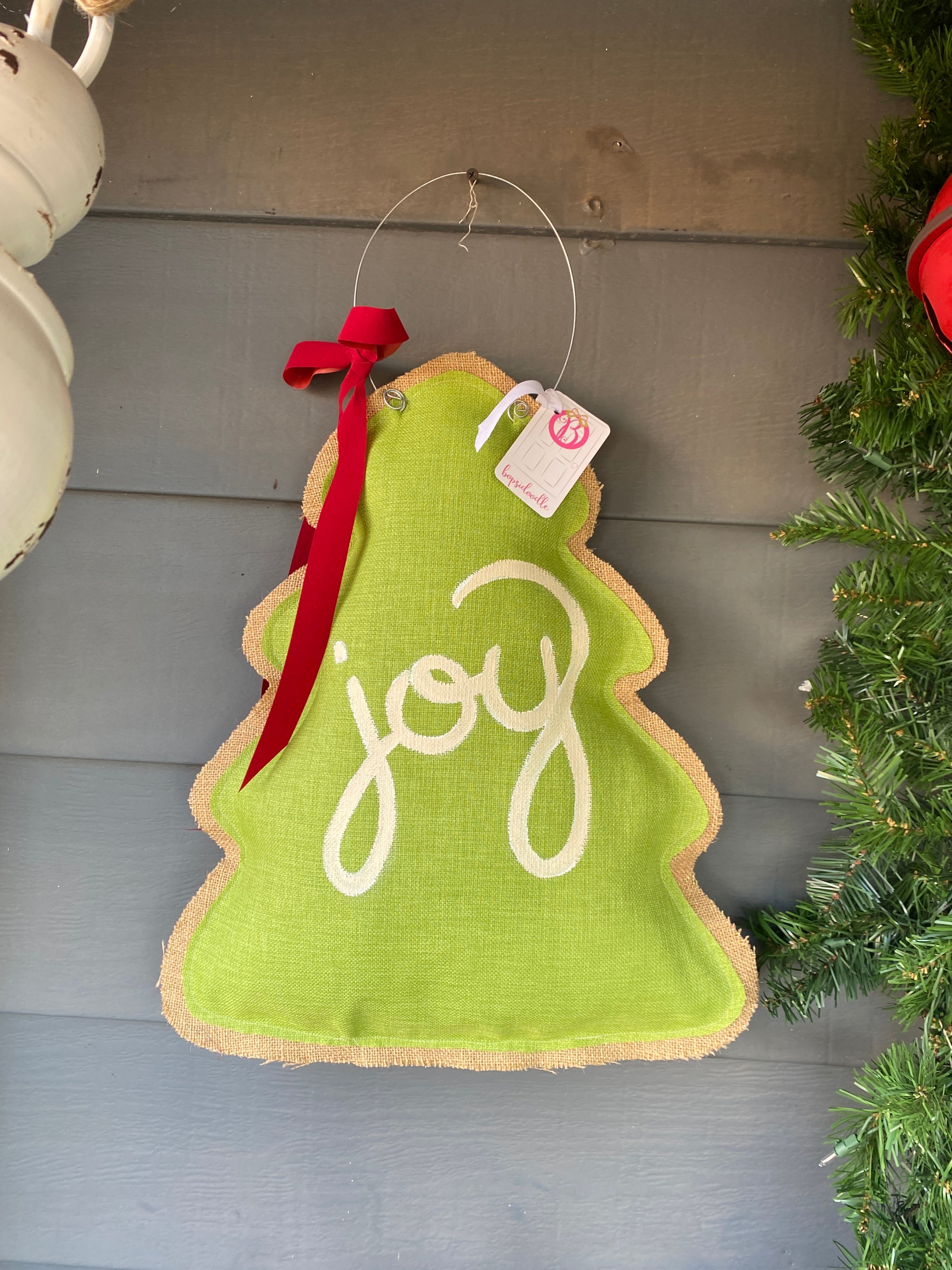What a fun way to brighten up your front door! This door hanger is green and tree shaped. It's accented with Joy lettering and a red bow. It's adorable!