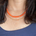 Double necklace featuring a gold oblong chain link necklace layered with an orange and gold beaded disc necklace.