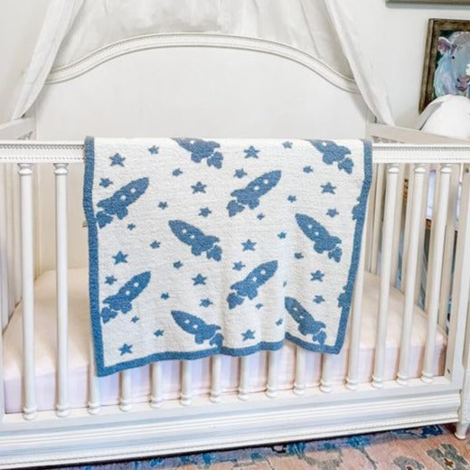 White blanket with blue trim and blue stars and rockets throughout